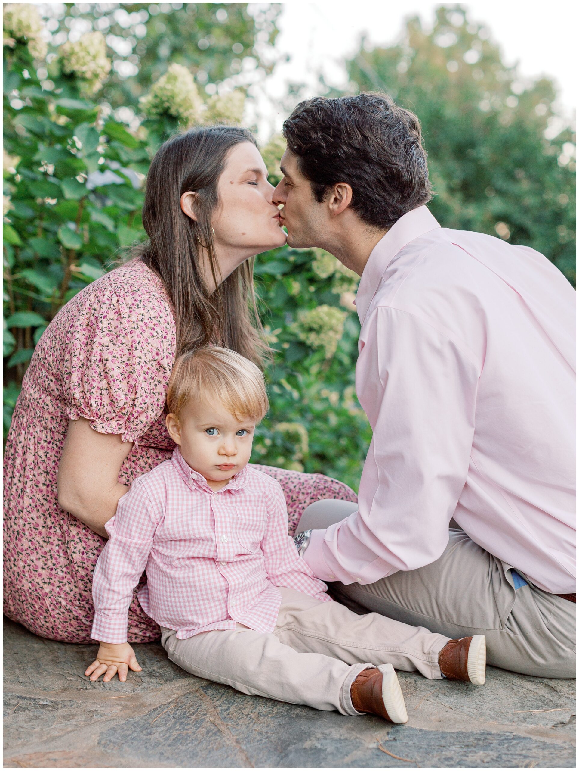 Parents kissing with their toddler making a funny face during a fall family maternity session at Bluemont Vineyard