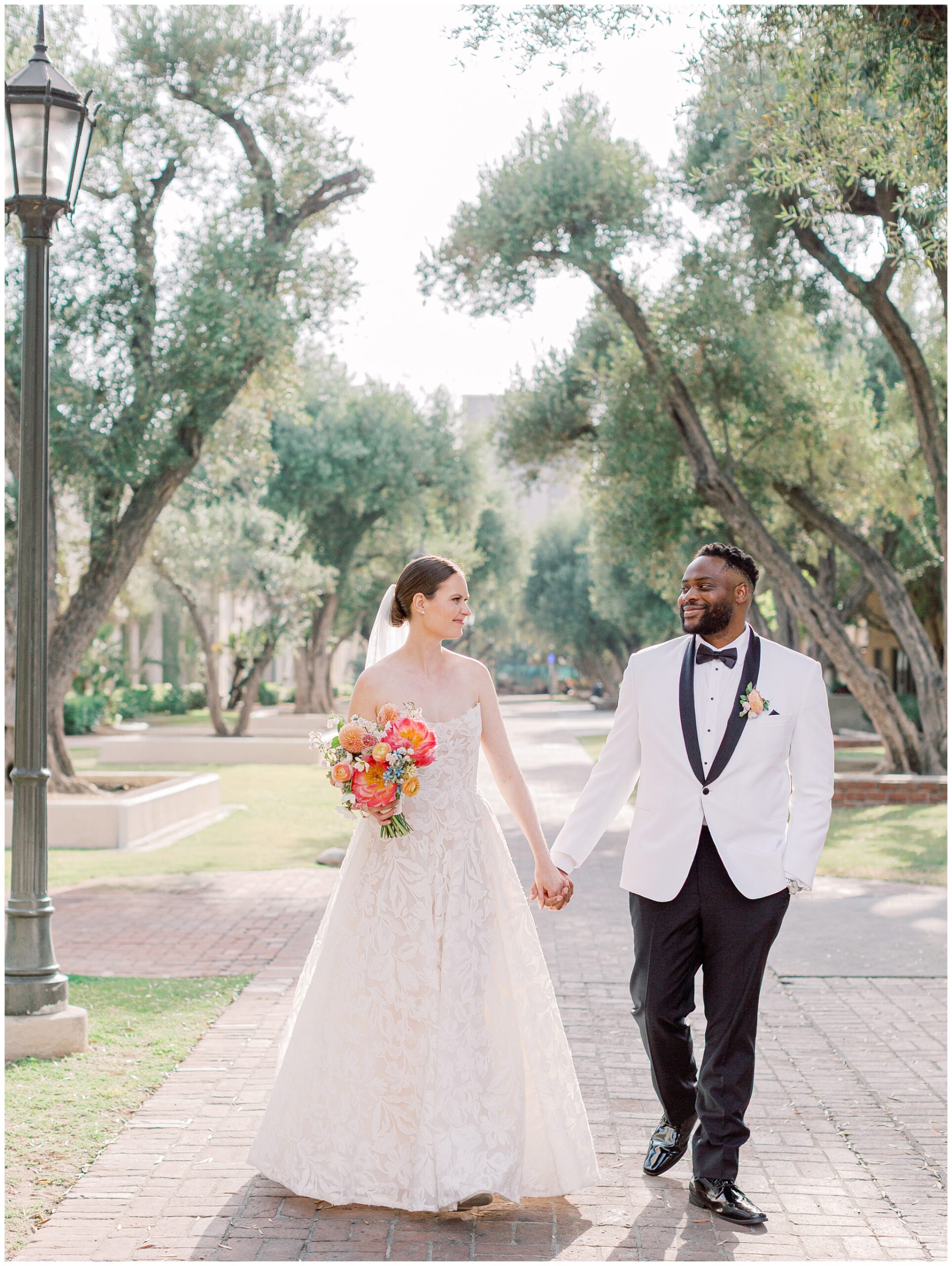 Bride and Groom walking on olive tree lined pathway at Caltech Athenaeum wedding