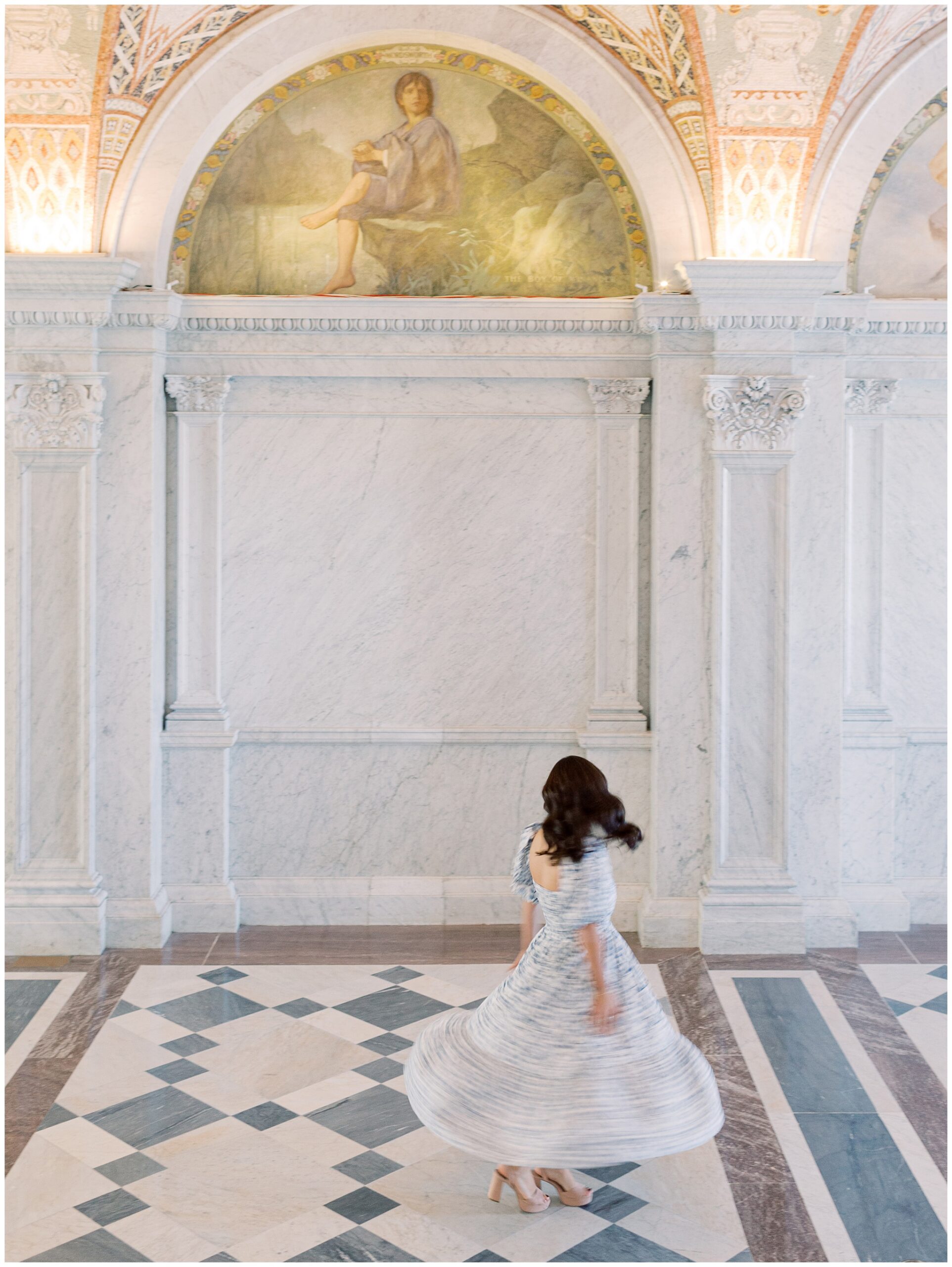 Maya twirling during her Library of Congress engagement session in Washington, DC, with soft motion blur and marble walls creating an old-world, romantic feel