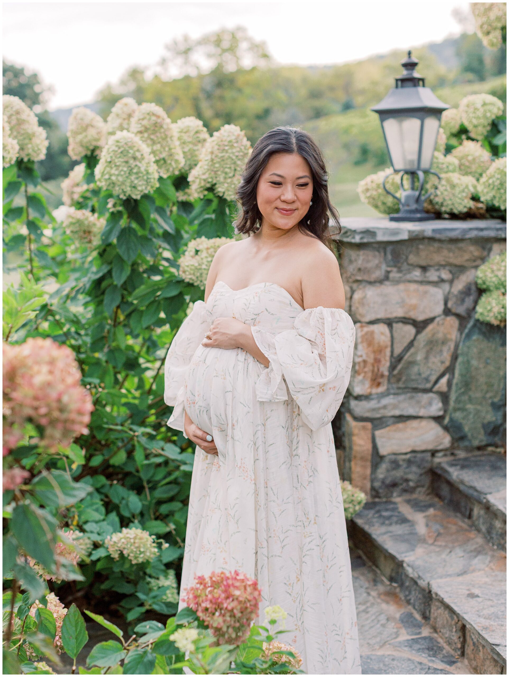 Jenny in a soft, flowy gown smiling during maternity photos at Bluemont Vineyard on the hydrangea lined staircase