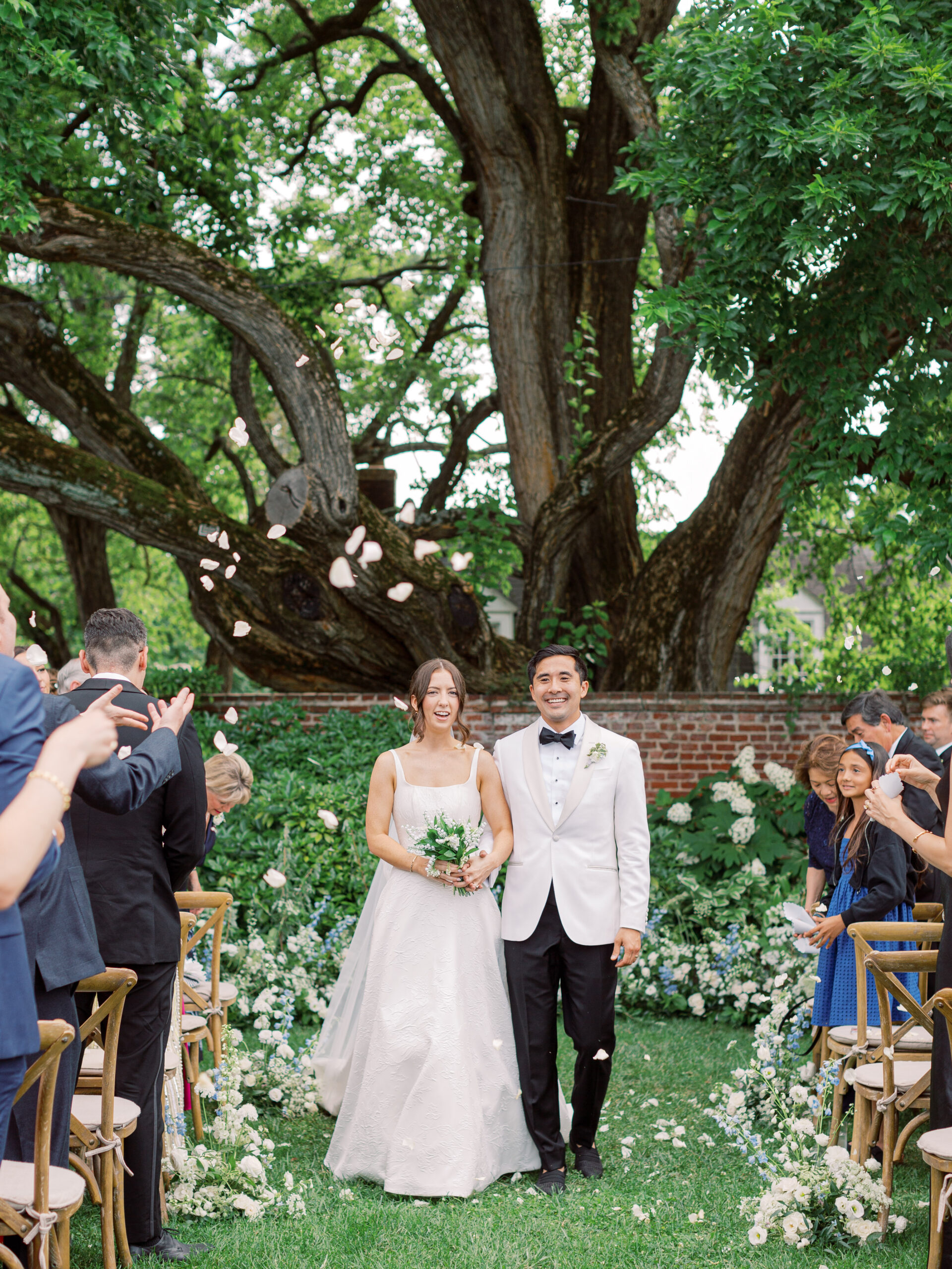Newlywed couple walking back down the aisle during their River Farm wedding as guests toss flower petals around them