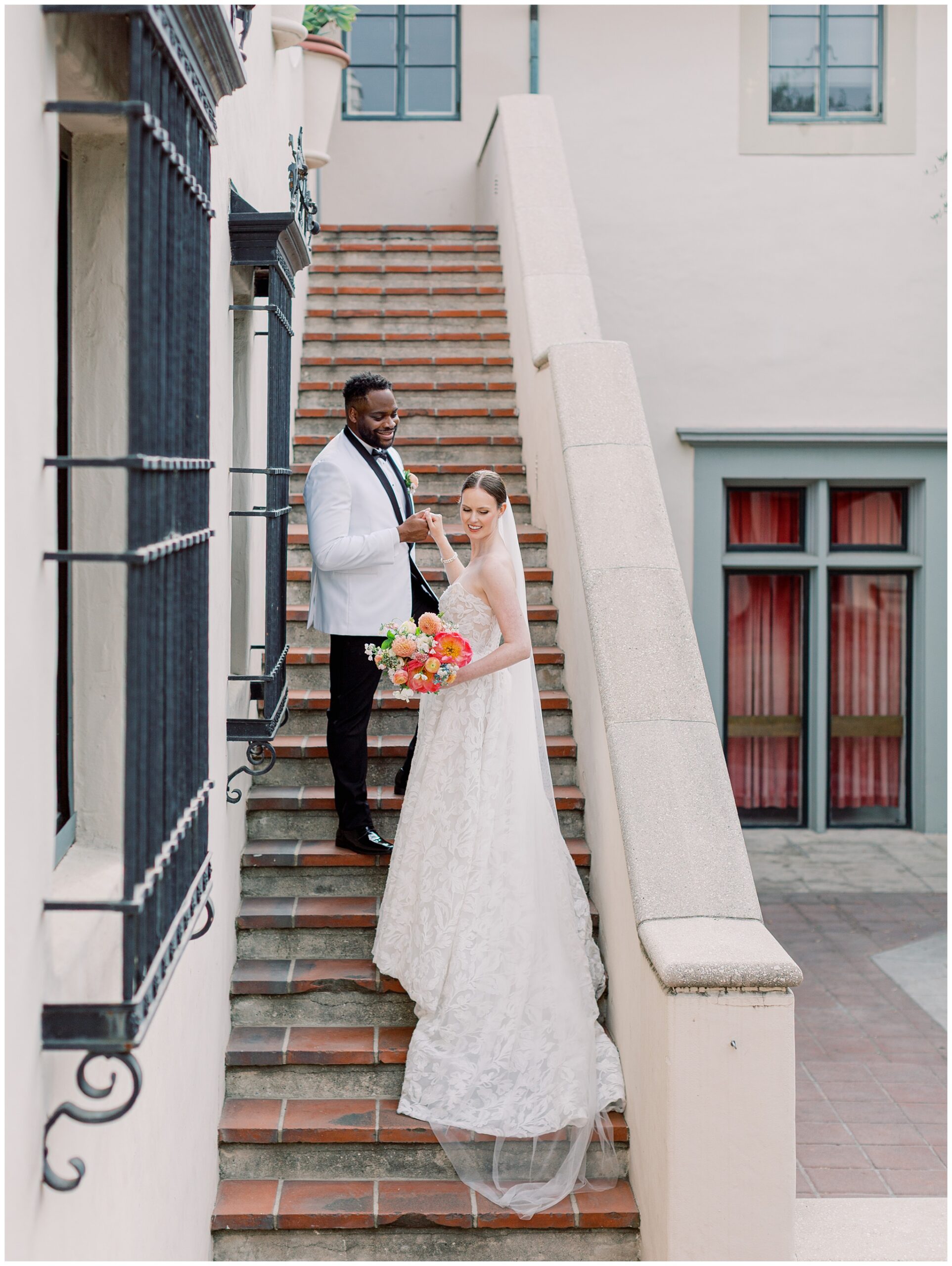 Groom helping bride up the staircase steps in the courtyard during their wedding portraits
