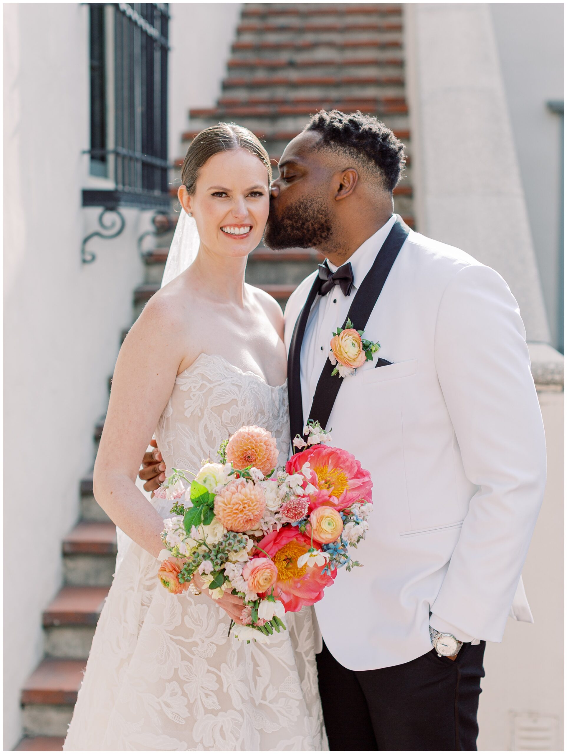 Groom kissing bride’s cheek during a wedding portrait in the courtyard