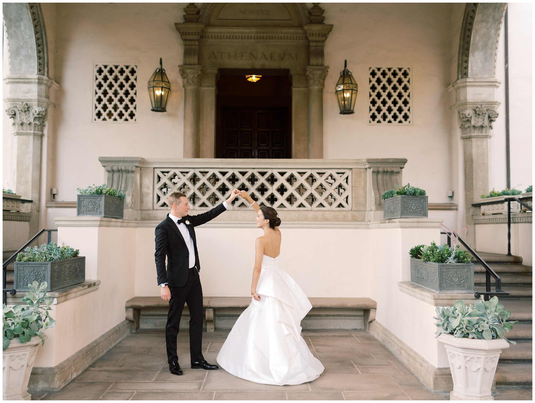 Groom twirling bride at the Athenaeum entrance during their wedding portraits