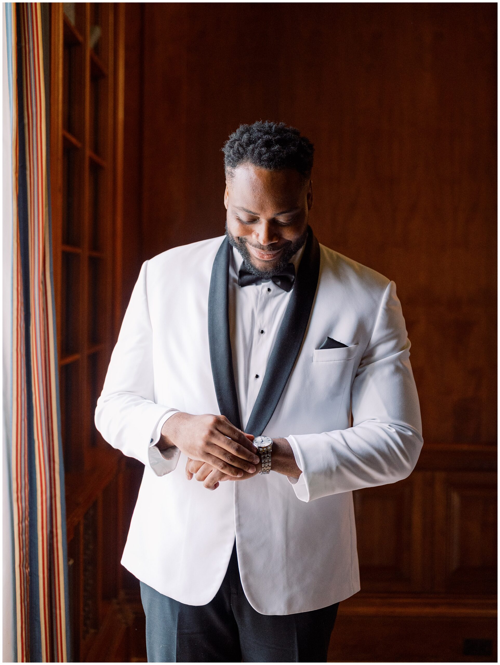 Groom adjusting his watch while getting ready in the Library before his wedding day