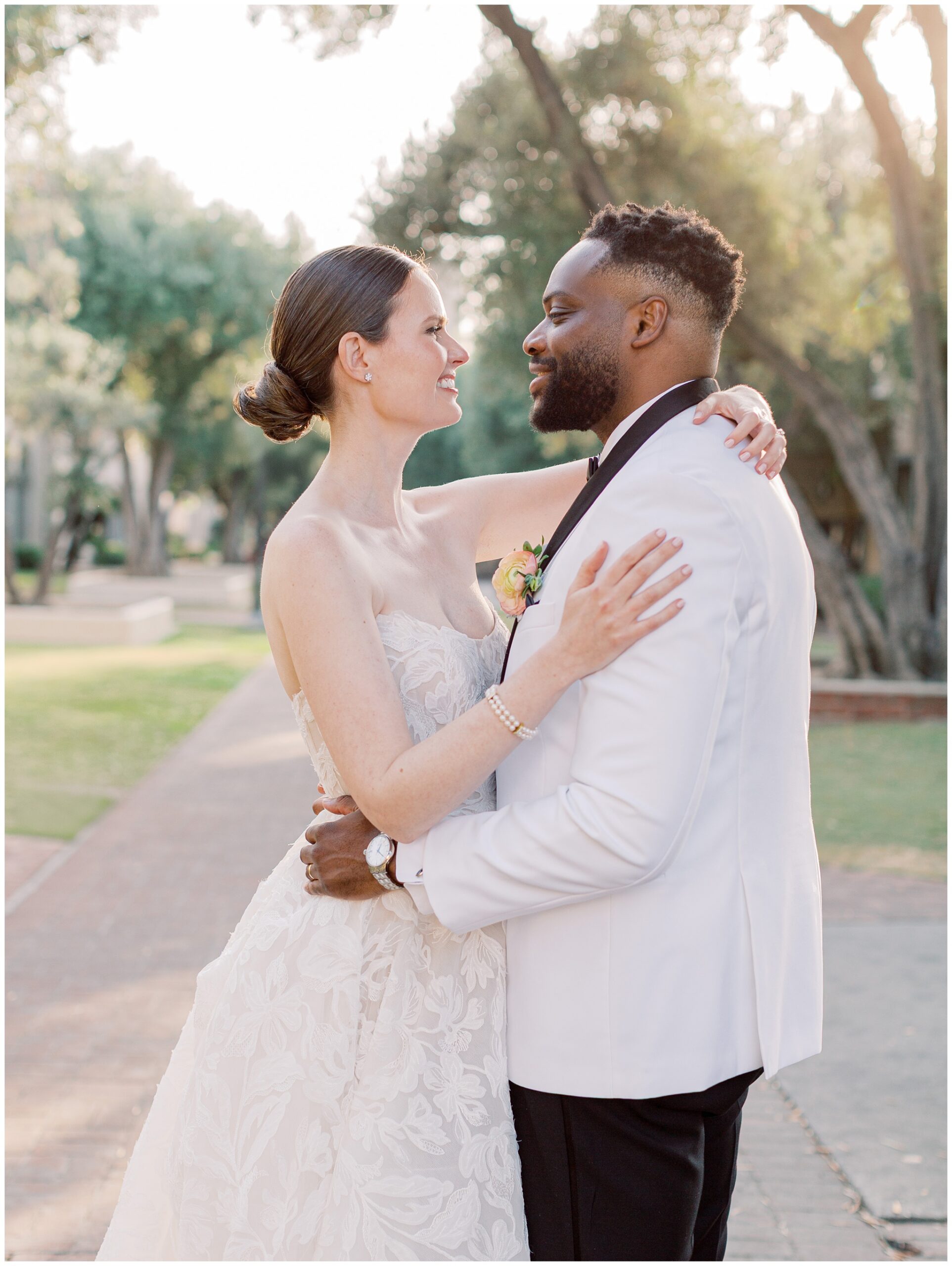 Bride and groom looking at each other in the olive tree-lined walkways at the Caltech Athenaeum during their wedding portraits