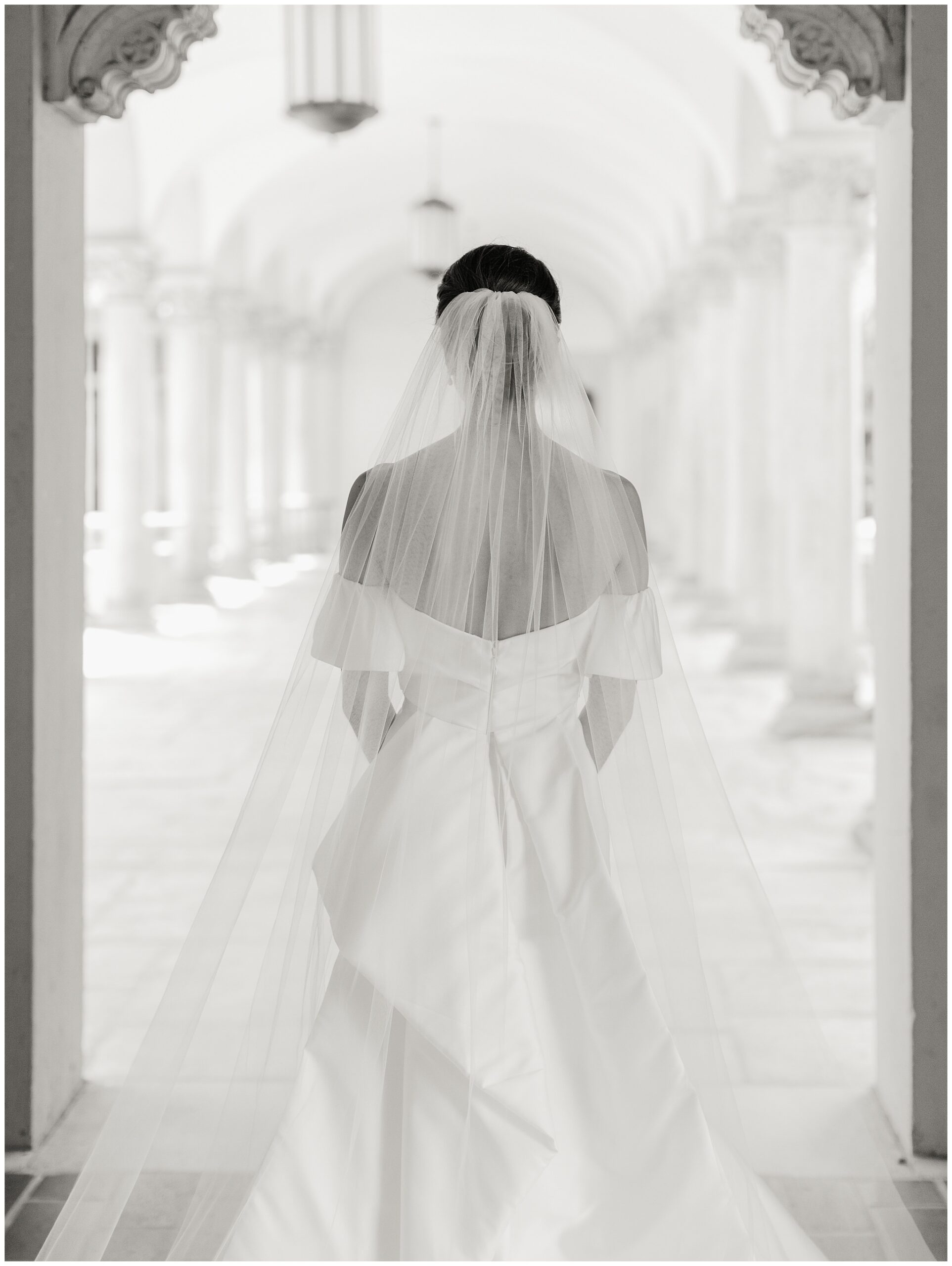 Black and white bridal portrait of bride walking beneath the columns at the Caltech Athenaeum