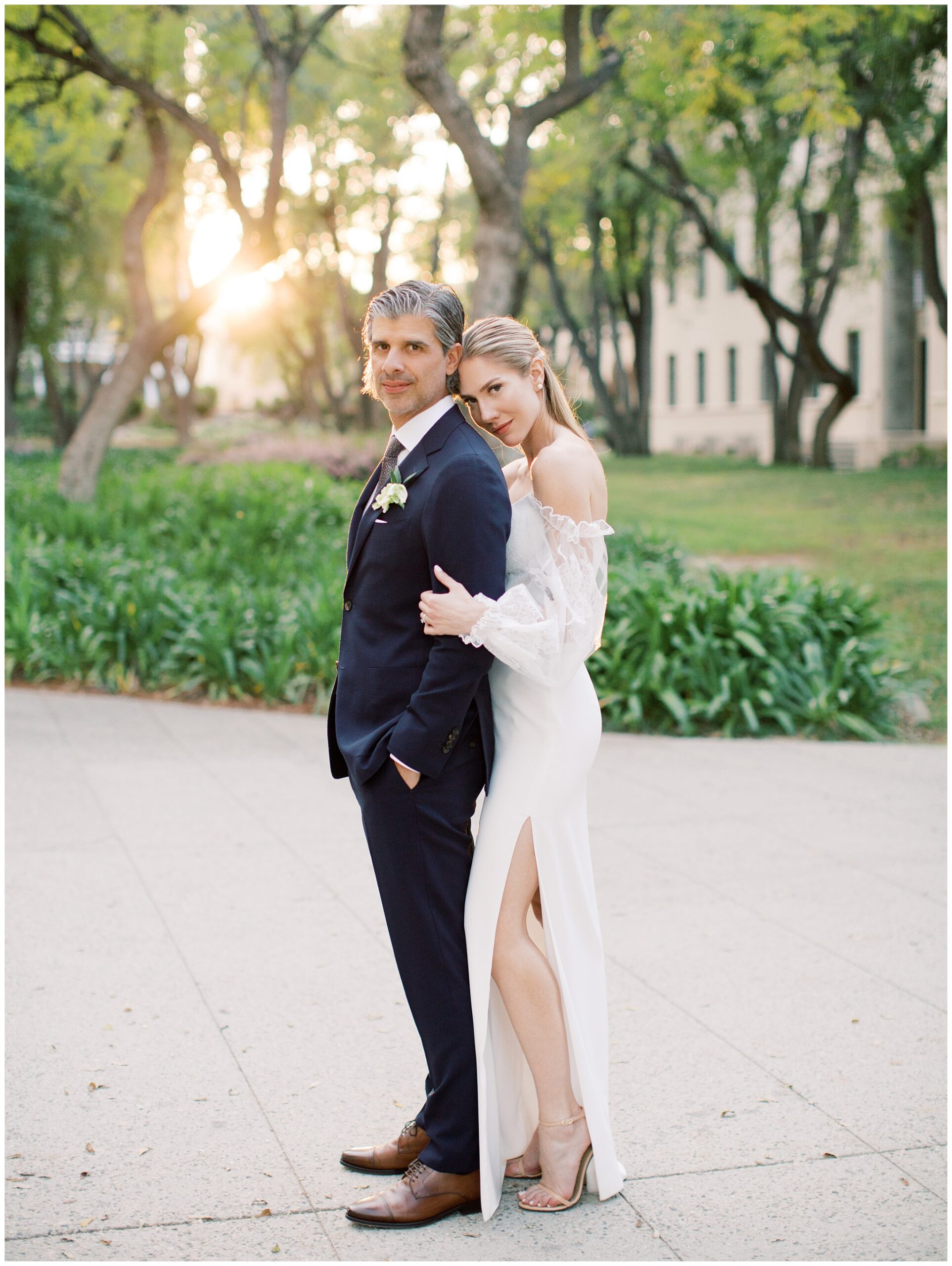 Bride holding the groom’s arm from behind during a sunset wedding portrait