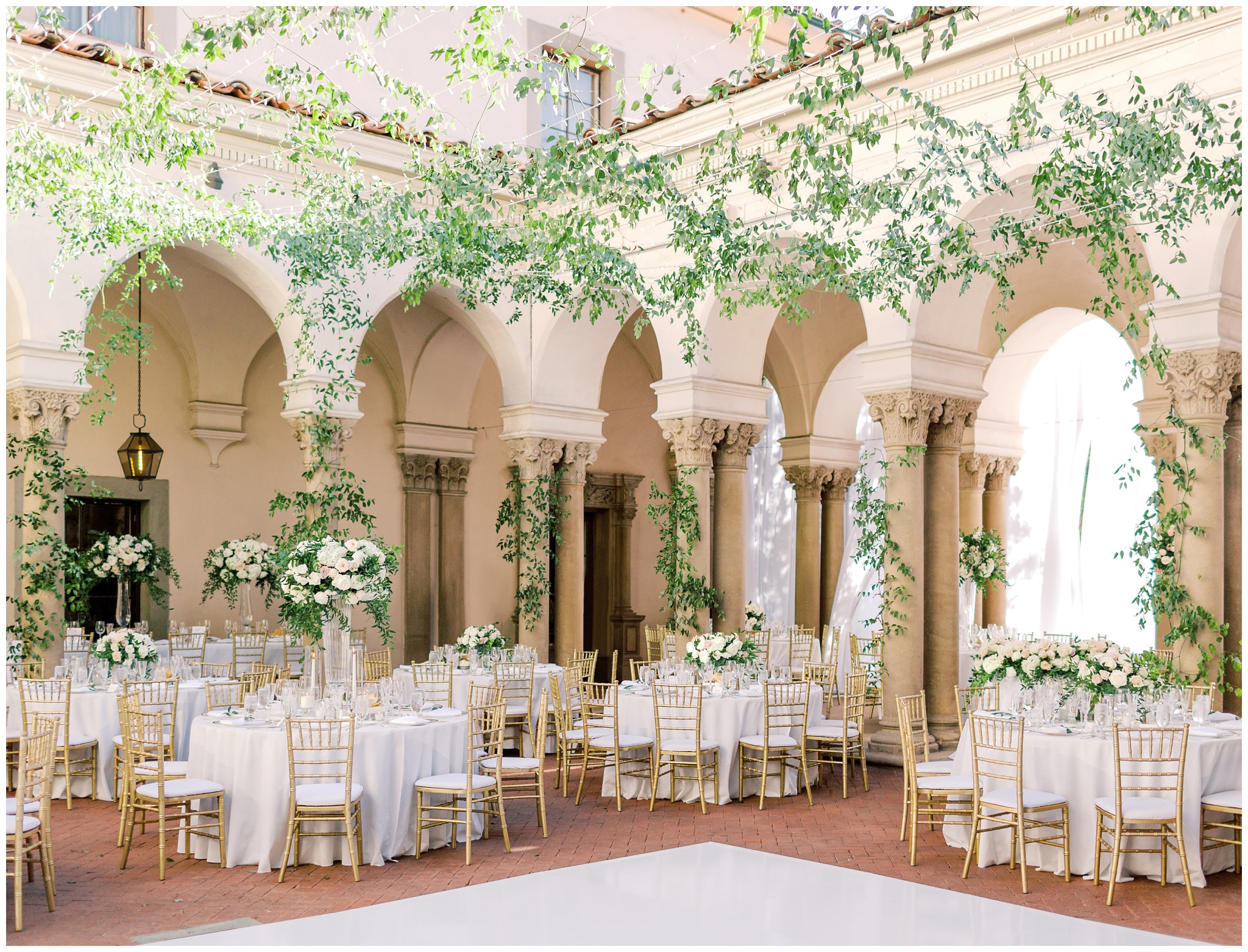 Wedding reception on the West Patio at the Caltech Athenaeum featuring lush floral arrangements, greenery cascading from the ceiling, and elegant dining tables beneath the columns