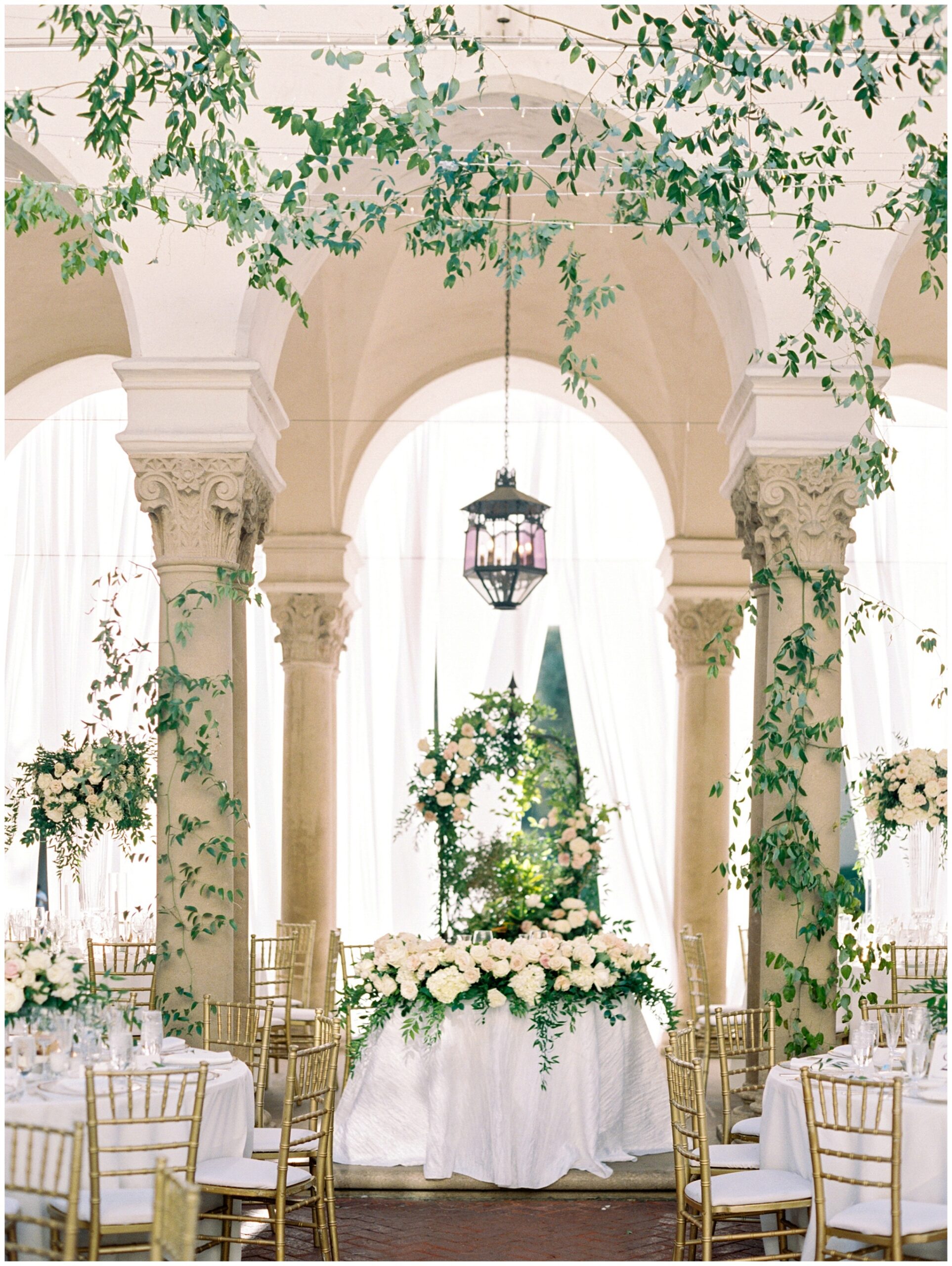 Newlywed sweetheart table on the West Patio at the Caltech Athenaeum surrounded by cascading greenery and abundant floral arrangements