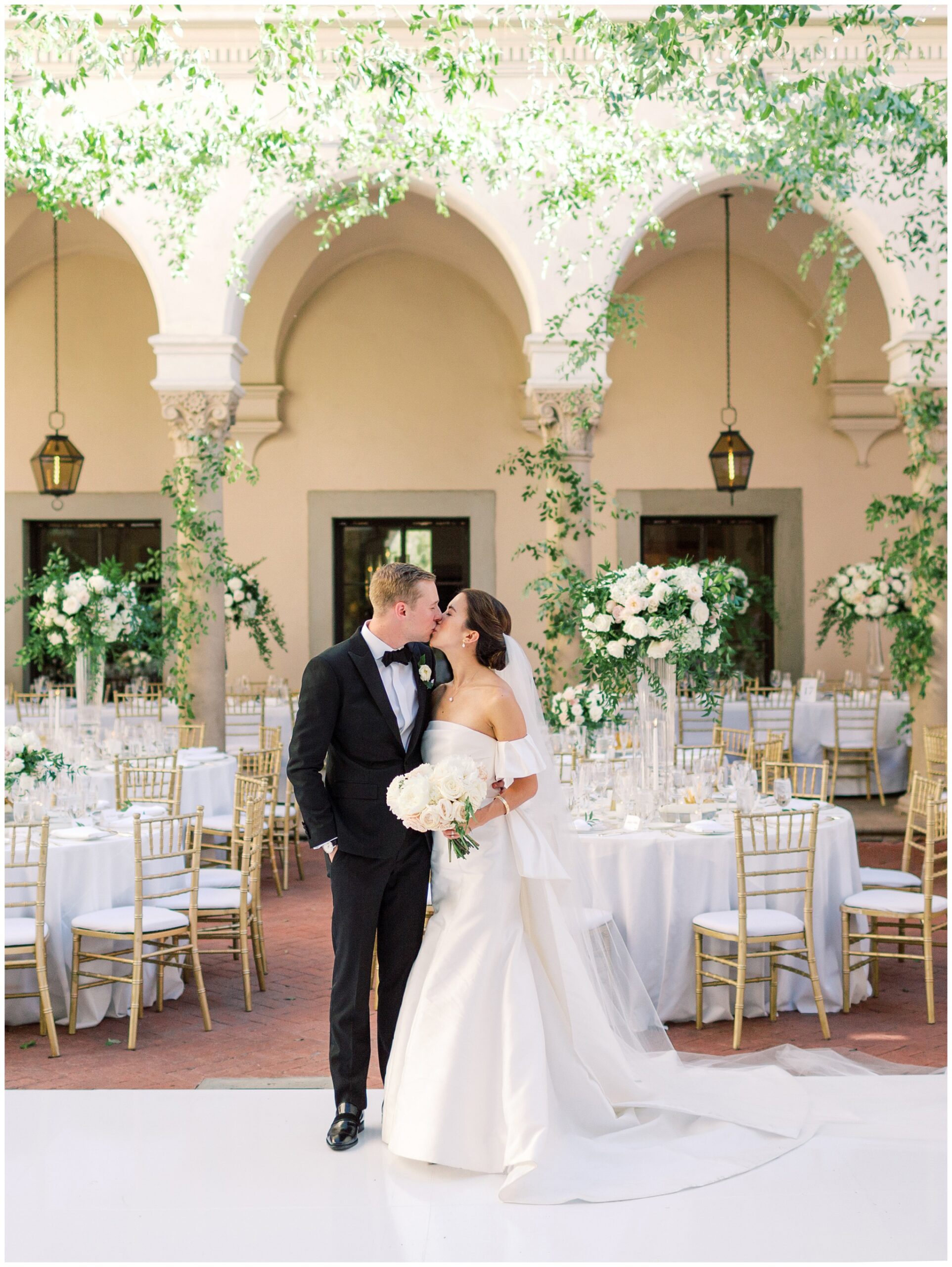 Newlywed couple kissing during their Caltech Athenaeum wedding reception surrounded by lush florals and greenery on the West Patio