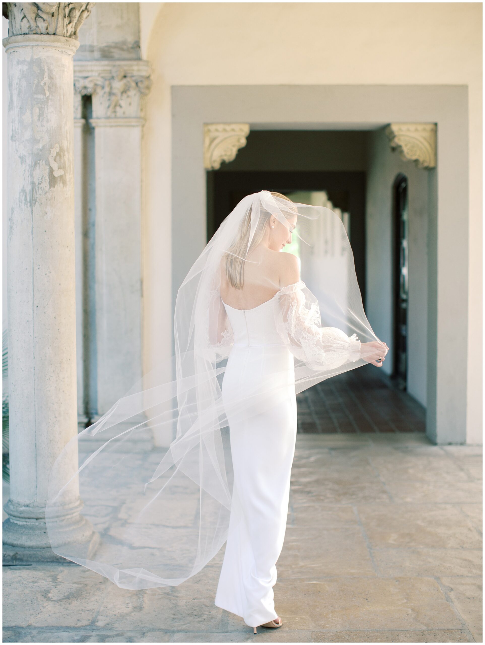Bride walking beneath the columns with her veil flowing behind her during a bridal portrait at the Caltech Athenaeum
