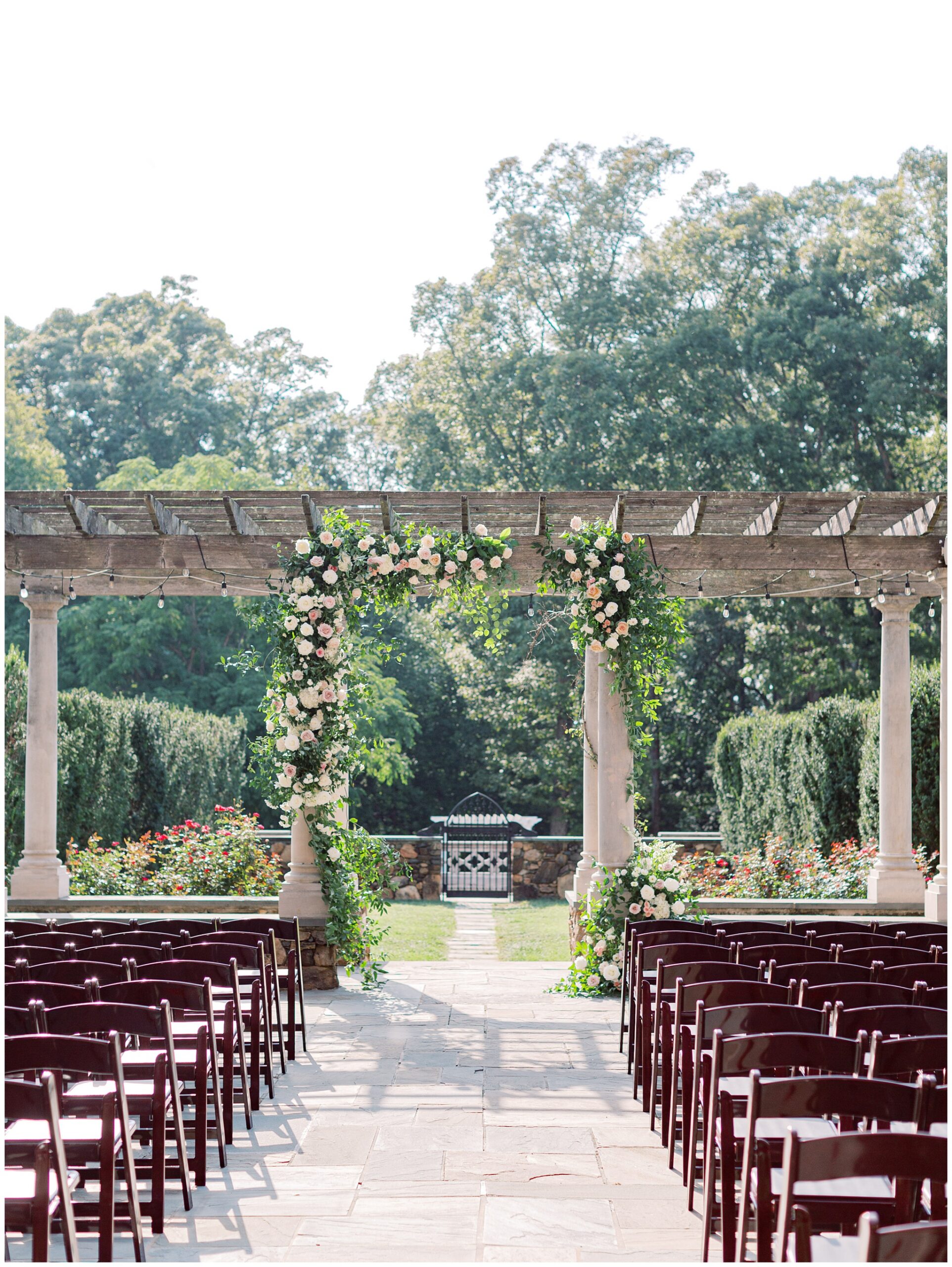 Wedding ceremony on the Bluestone Terrace featuring a grand floral arch climbing the stone columns