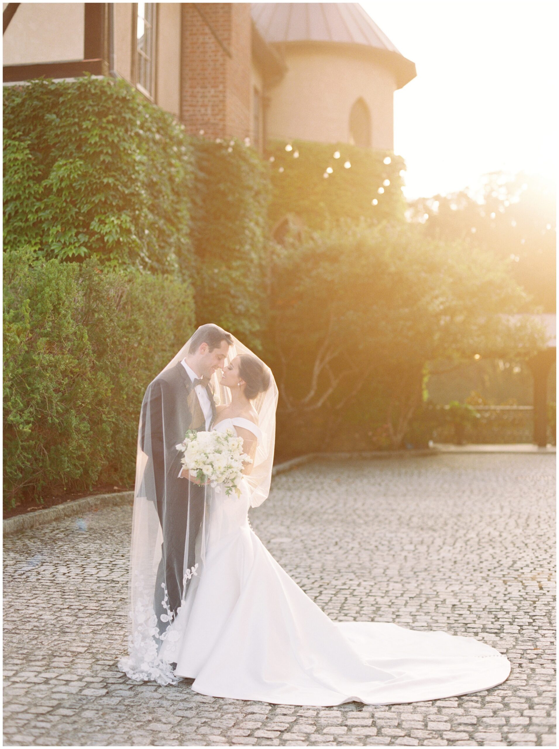 Bride and groom sharing a romantic moment beneath the veil in the cobblestone court at Dover Hall during golden hour