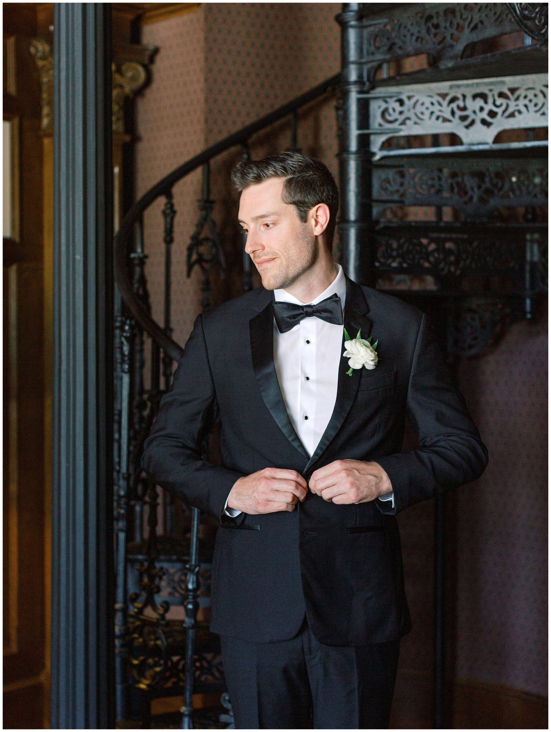 Groom buttoning his jacket during a portrait in the Library