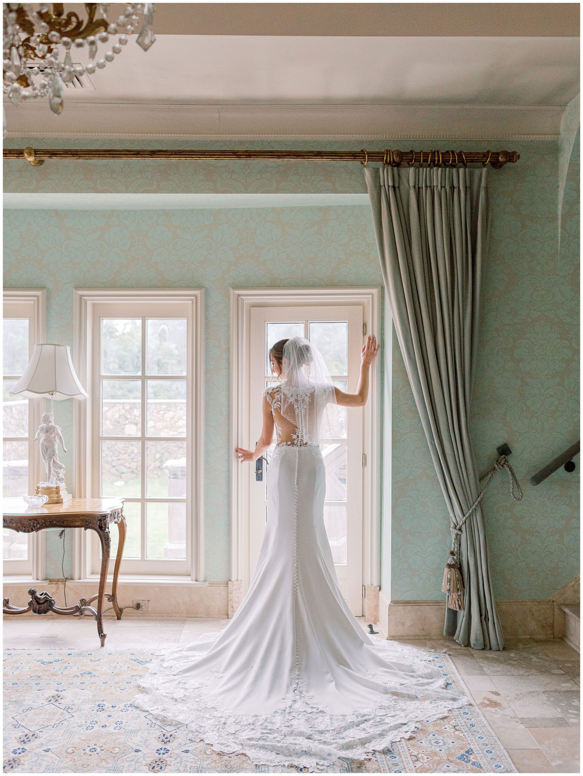 Bridal portrait of a bride standing in front of tall windows in an elegant room
