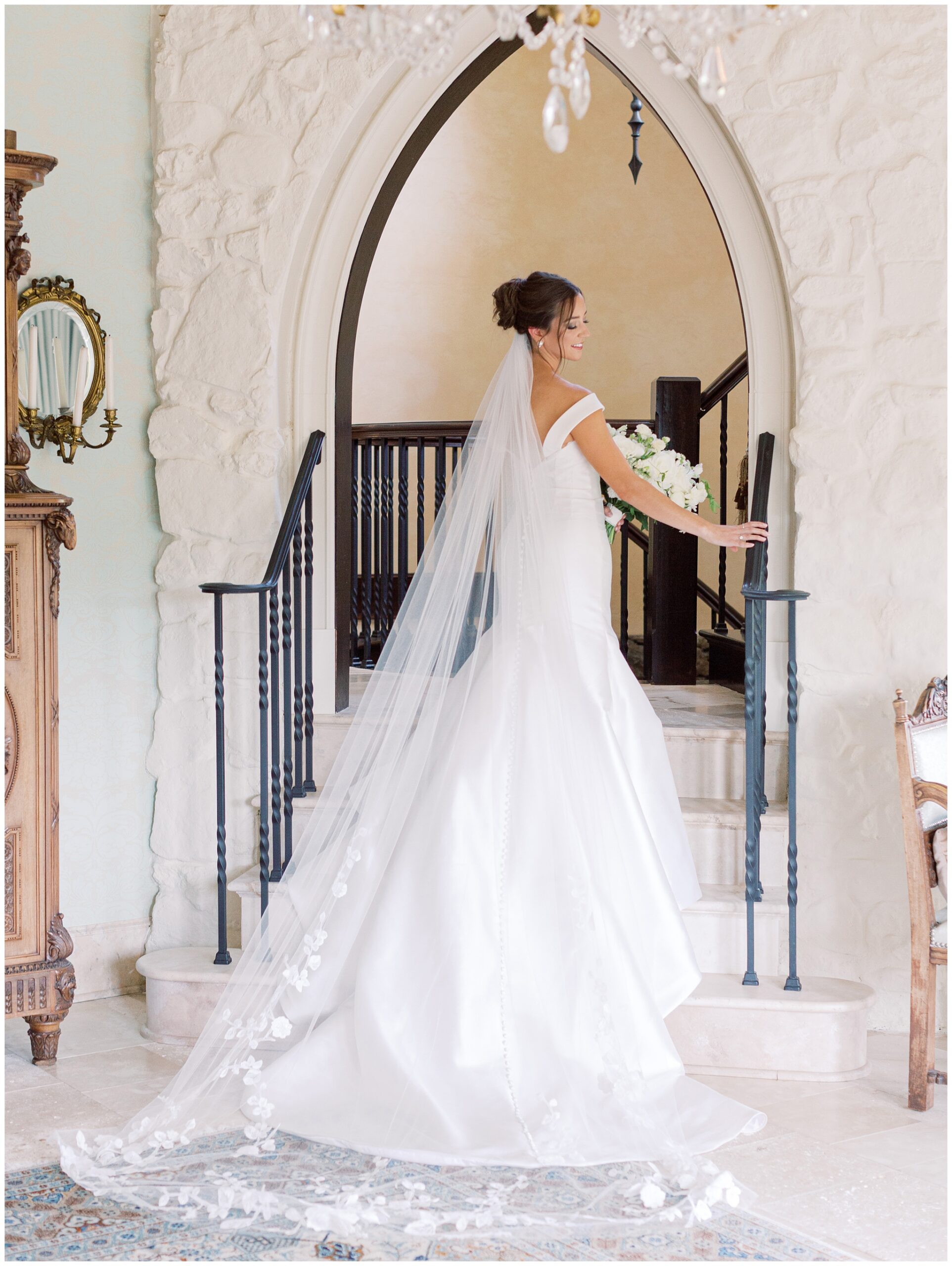 Bridal portrait of a bride standing at the bottom of the spiral staircase at Dover Hall with her hand resting on the banister