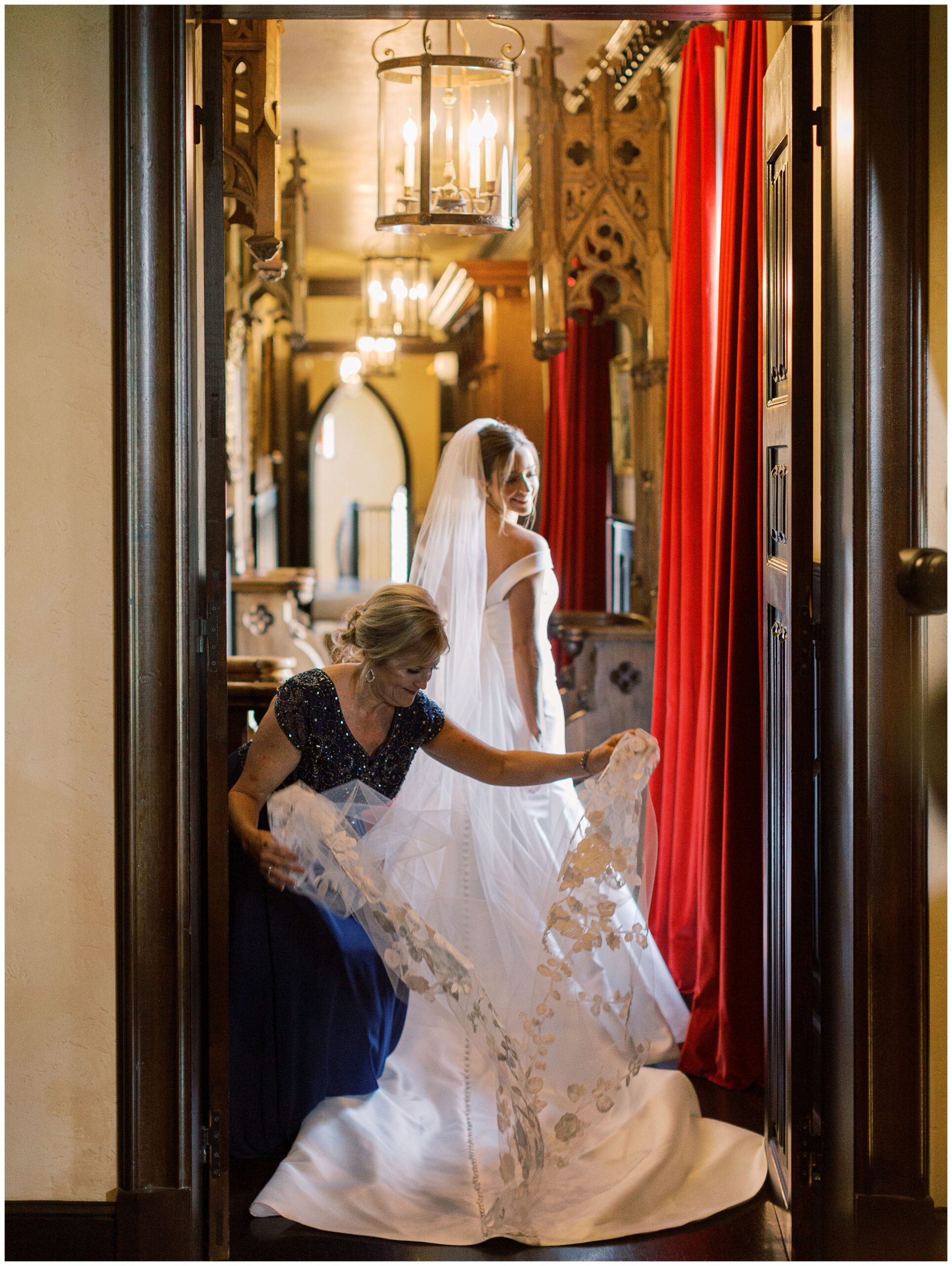 Bride’s mother adjusting the bride’s wedding dress in an ornate hallway before the ceremony