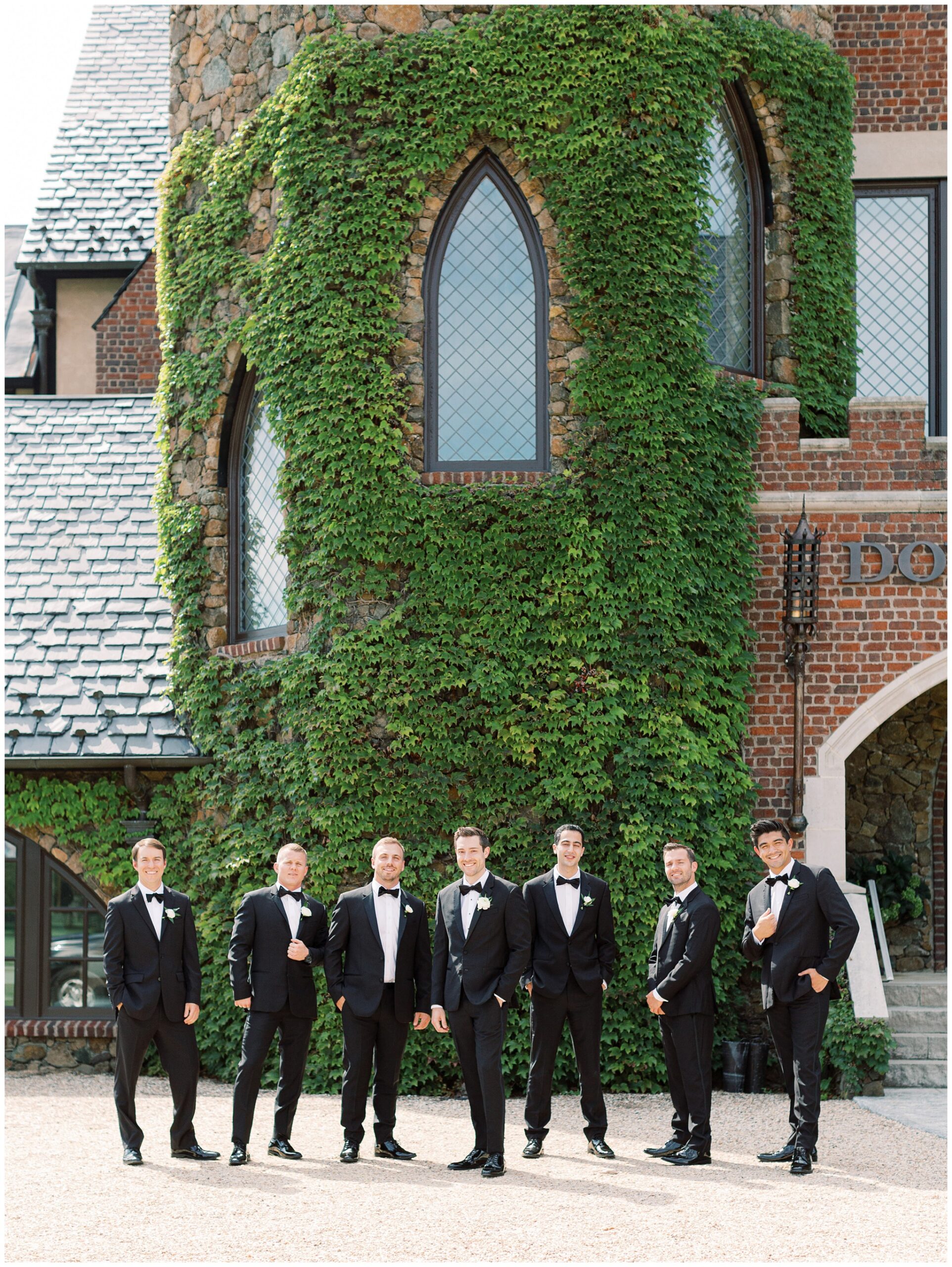 Groom and groomsmen posing beside the ivy-covered turret