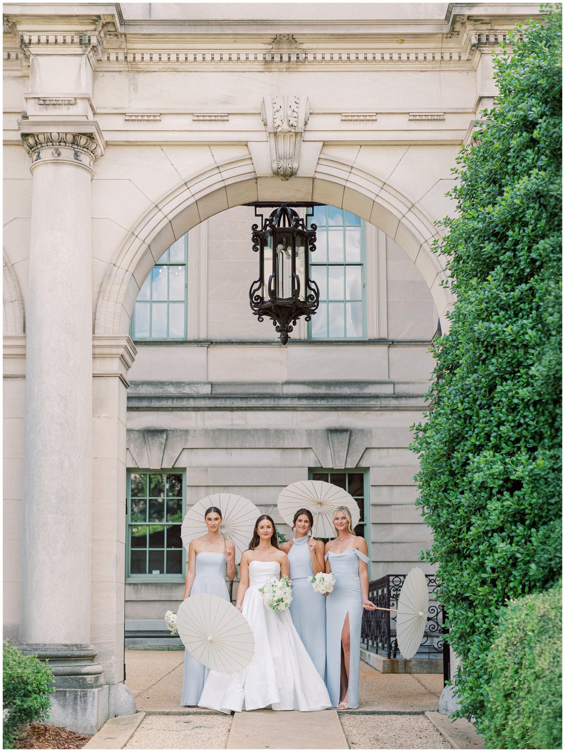 Bride standing with bridesmaids in pale blue dresses and parasols outside Anderson House
