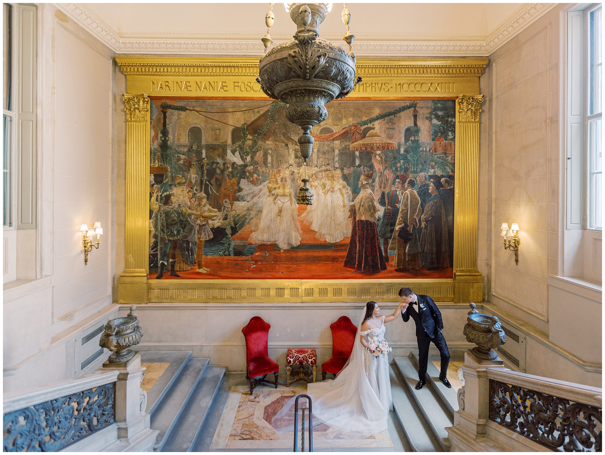 Groom kissing bride’s hand on the Great Stair Hall staircase at Larz Anderson House wedding