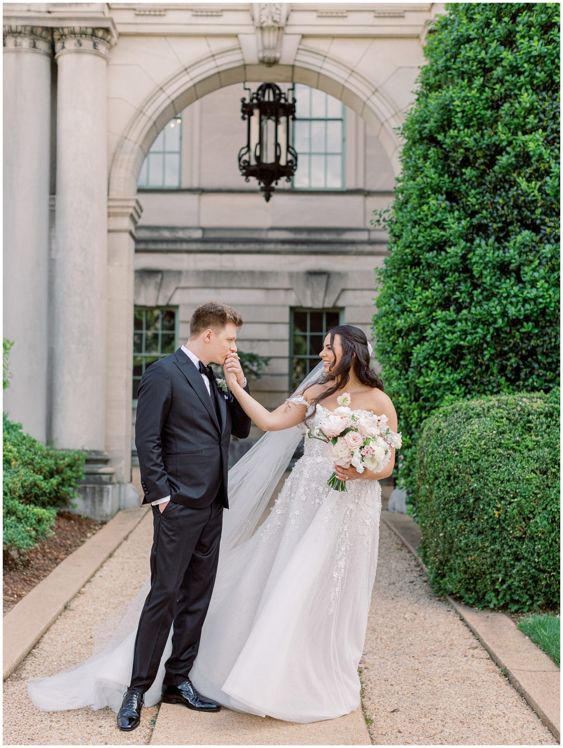 Groom kissing bride's hand at the front entrance of Anderson House